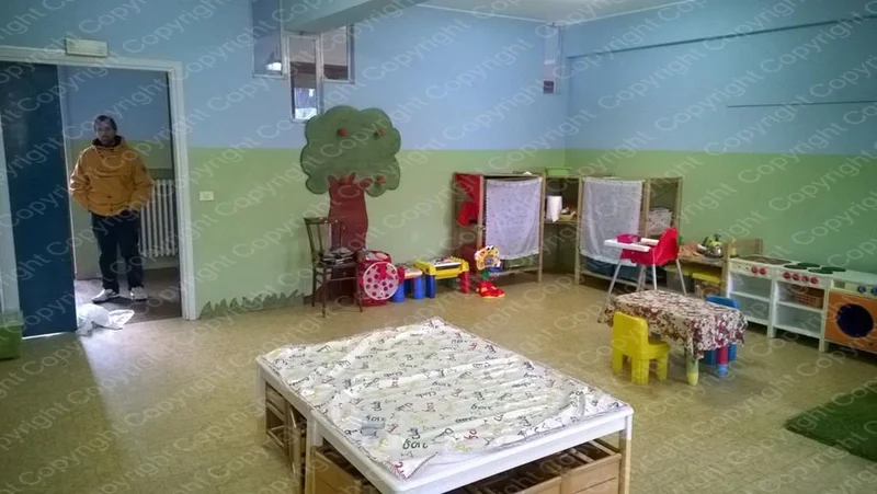Sala con lettino, albero dipinto sul muro e angolo lettura con libri e giochi