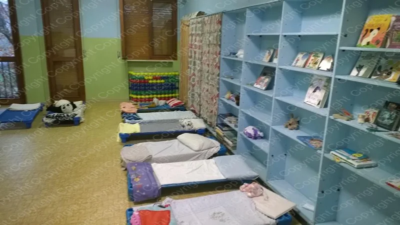 Sala riposo del Centro Prima Infanzia con brandine pieghevoli e scaffali con libri e giochi